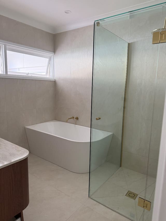 Freestanding bath beside a frameless glass shower with brushed brass fittings