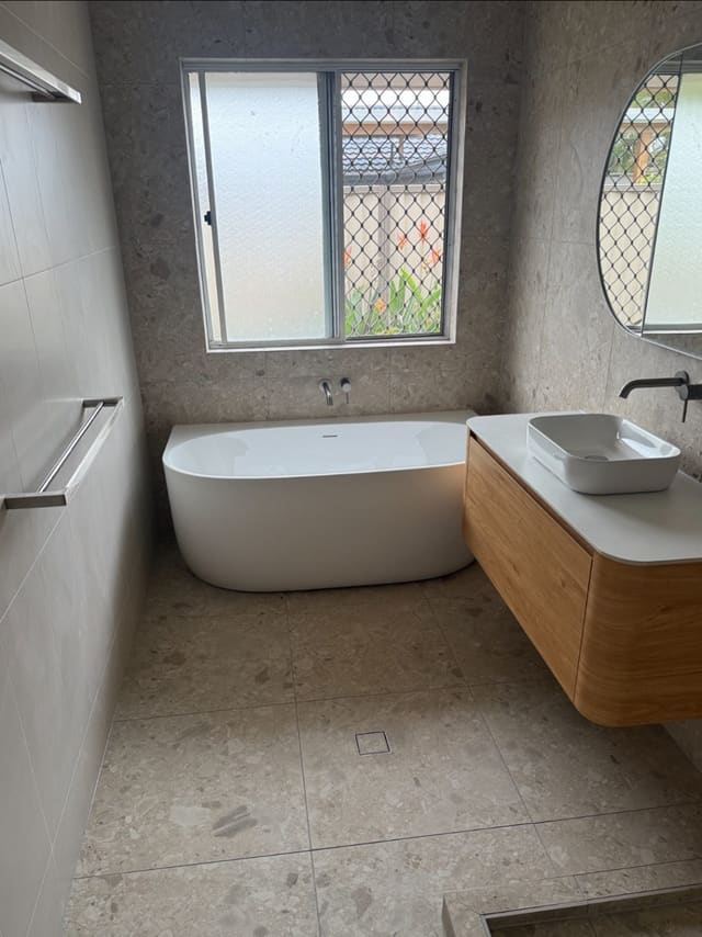 Freestanding bath and fluted timber vanity with a vessel basin under a window