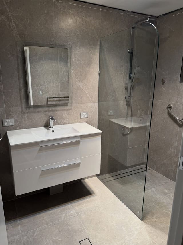 Frameless shower with grab rails beside a white wall-hung vanity