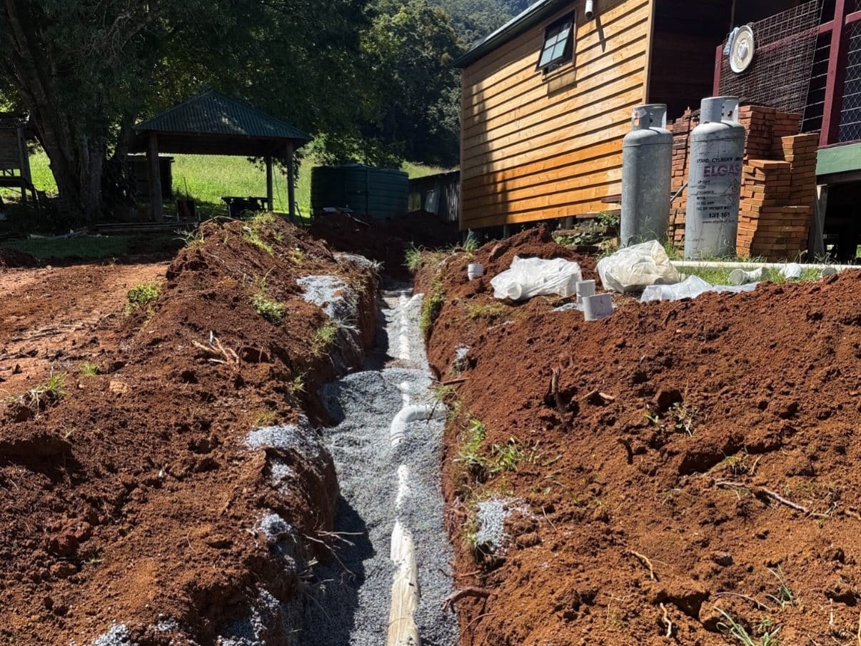 New drainage pipe bedded in gravel along an open trench beside a house