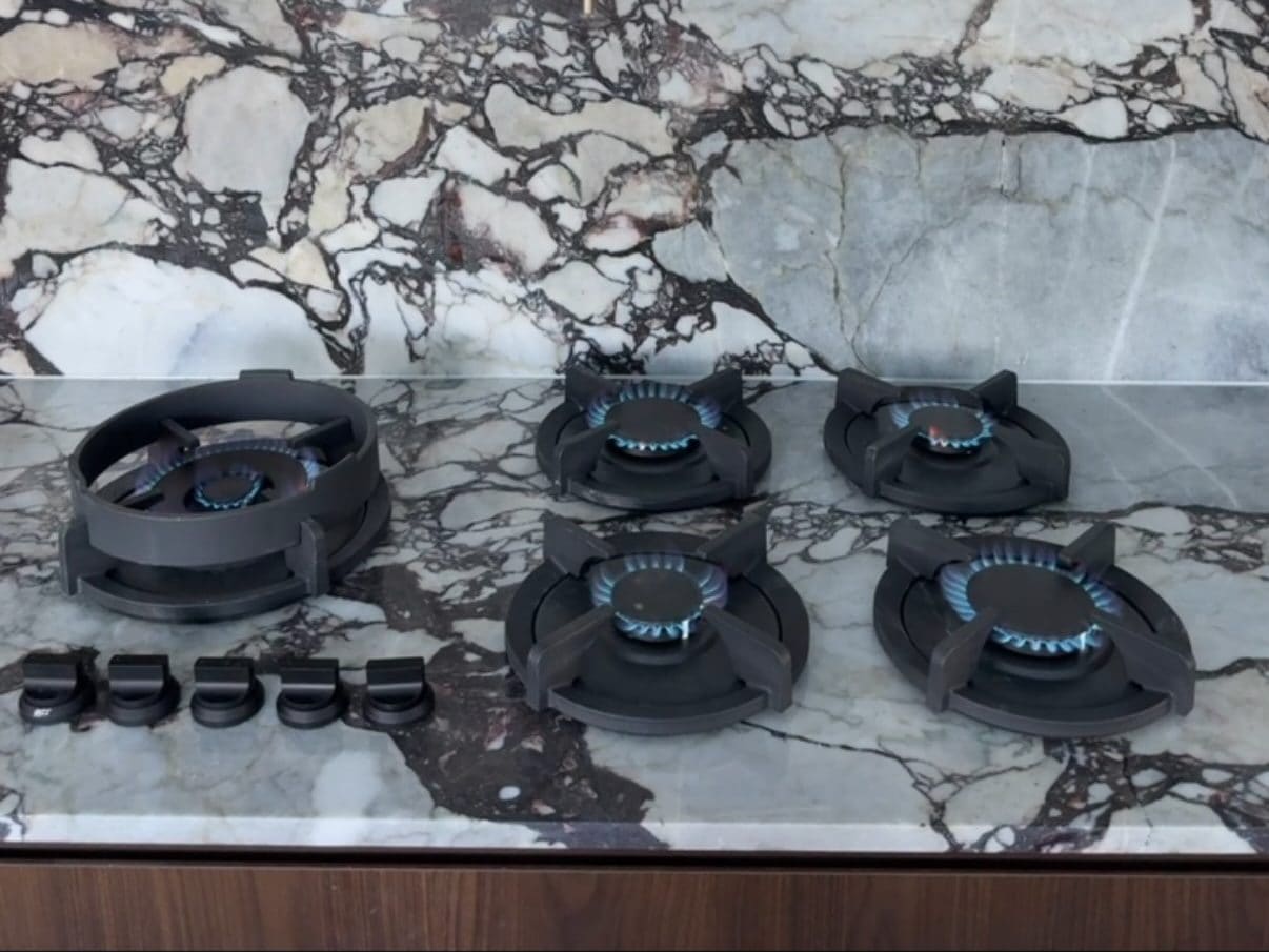 Five-burner gas cooktop with all burners lit on a marble benchtop
