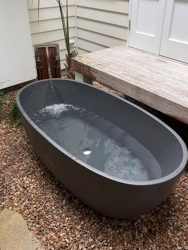 Freestanding stone bath filling from a wall spout in an outdoor courtyard