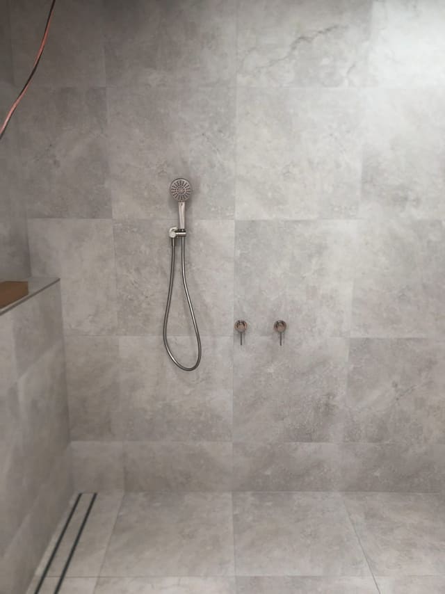 Tiled walk-in shower with a hand shower on a rail and a linear floor drain
