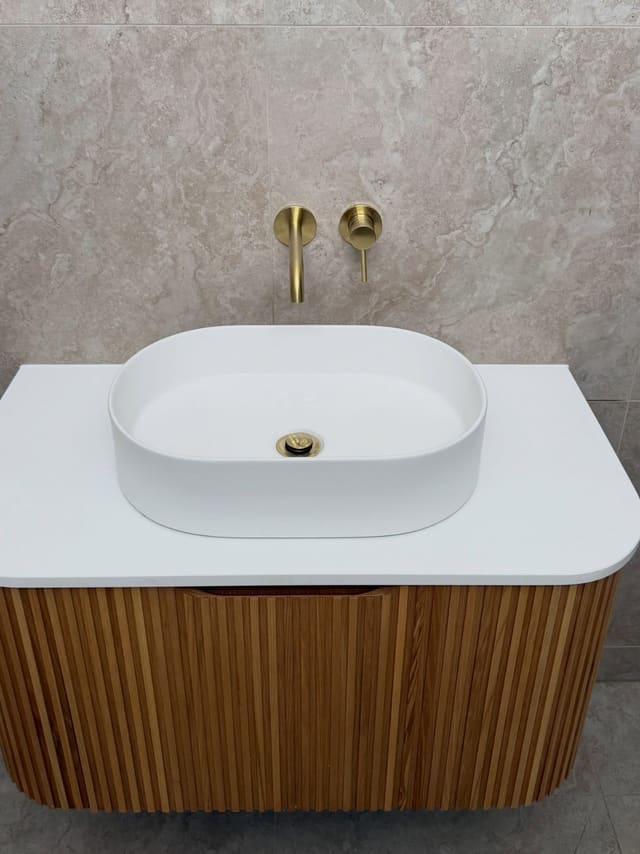Fluted timber wall-hung vanity with a white basin and brushed brass wall mixer